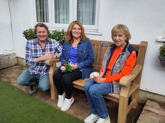 teak garden bench with 2 ladies seated on it on a patio with grass lawn