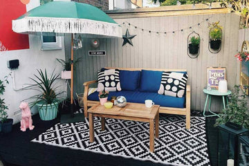teak garden bench with blue cushions on a decked area with green umbrella and beach theme background