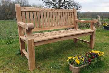 teak garden bench with engraving on a lawn with flowers in front