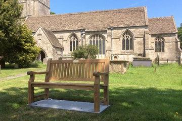 teak garden bench with a brass plaque in the grounds of an English church in the summer