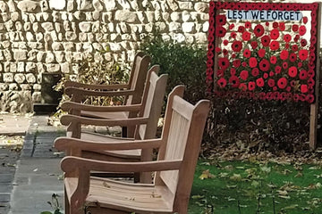 teak wooden benches in a row on a street with 'lest we forget' written in poppies in the background