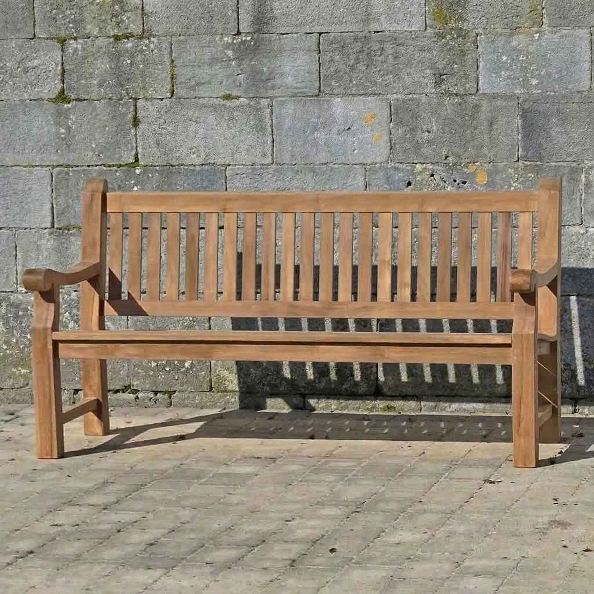 FSC 4 seat Teak Wooden garden bench in front of a stone wall
