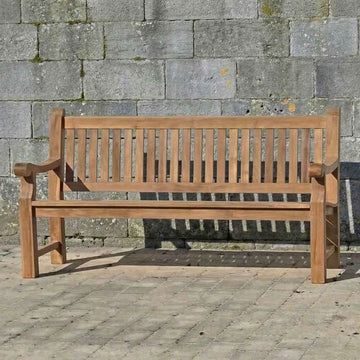 FSC 4 seat Teak Wooden garden bench in front of a stone wall