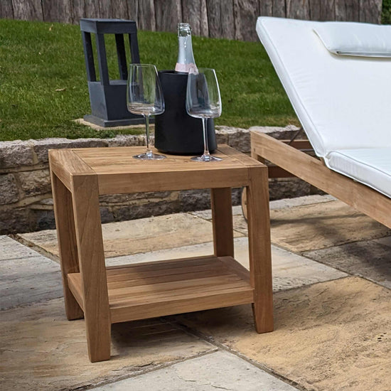 Wooden garden side table, shelf with wine glasses and a bottle on a patio