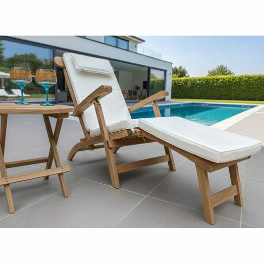 Wooden lounge steamer chair with white cushion next to a poolside table with drinks.