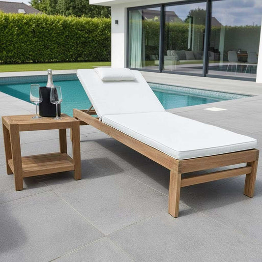 Wooden sun lounger chair with white cushion next to a poolside table with wine glasses and a bottle.