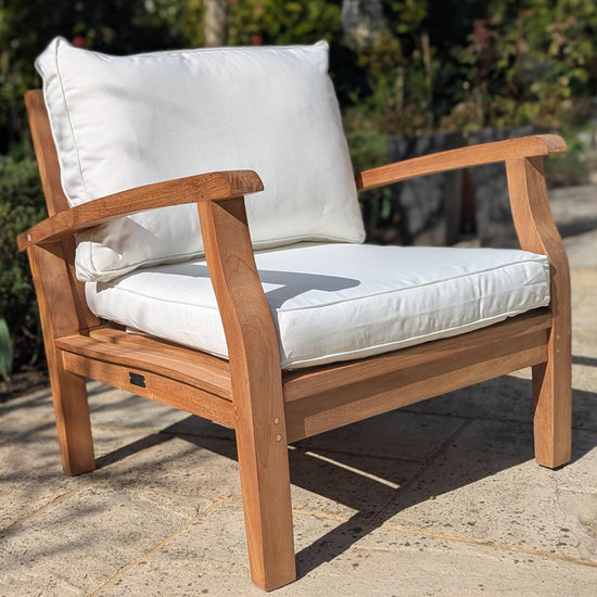 Wooden outdoor chair with white cushions on a stone patio