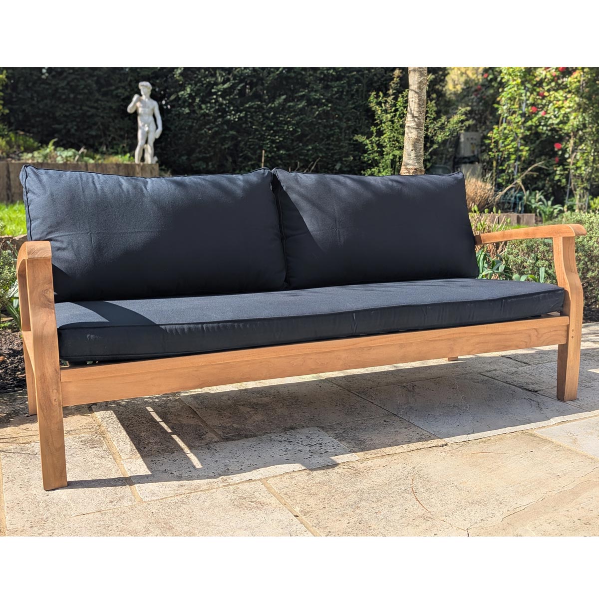 Wooden outdoor sofa with dark cushions on a stone patio