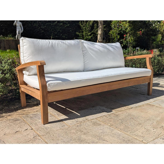 Wooden outdoor sofa with white cushions on a stone patio