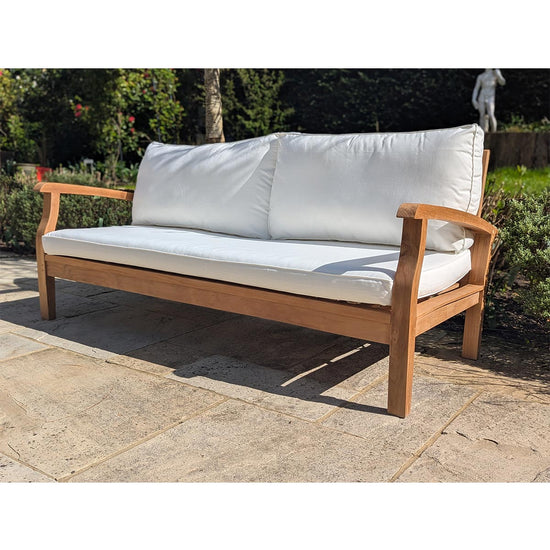 Wooden outdoor sofa with white cushions on a stone patio