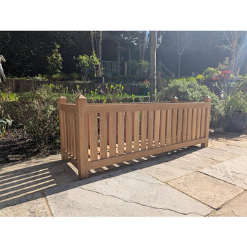 Wooden teak planter box on a patio with garden and trees in the background