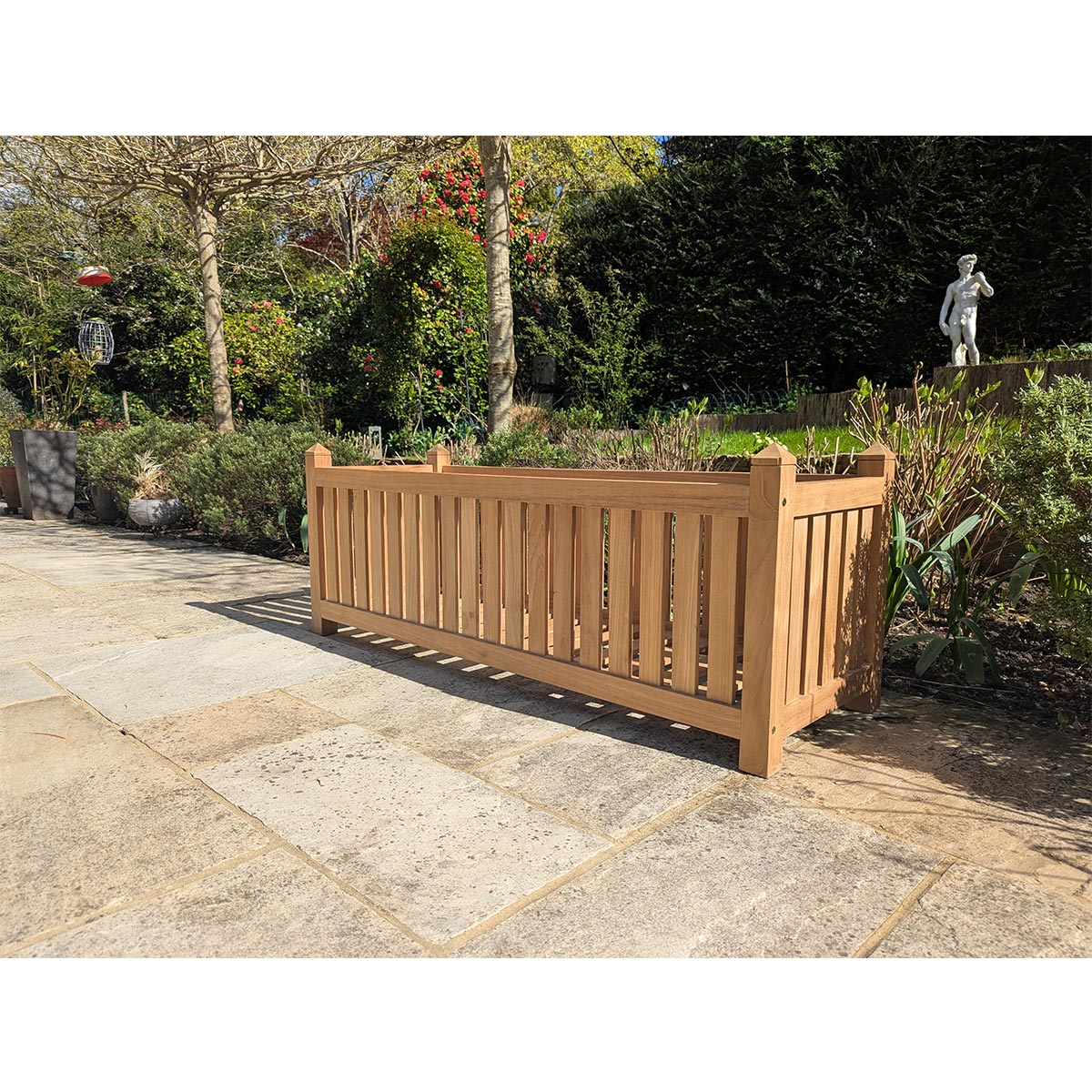 Wooden planter box in a garden setting with trees and a statue in the background