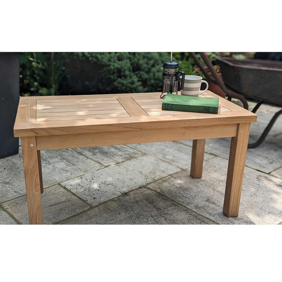 Low wooden teak outdoor table with a mug and book on a stone patio