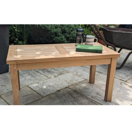 Low wooden teak outdoor table with a mug and book on a stone patio