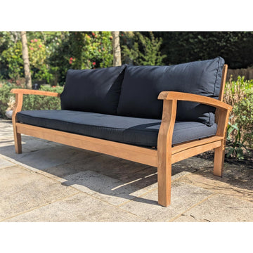 Wooden outdoor sofa with dark cushions on a stone patio