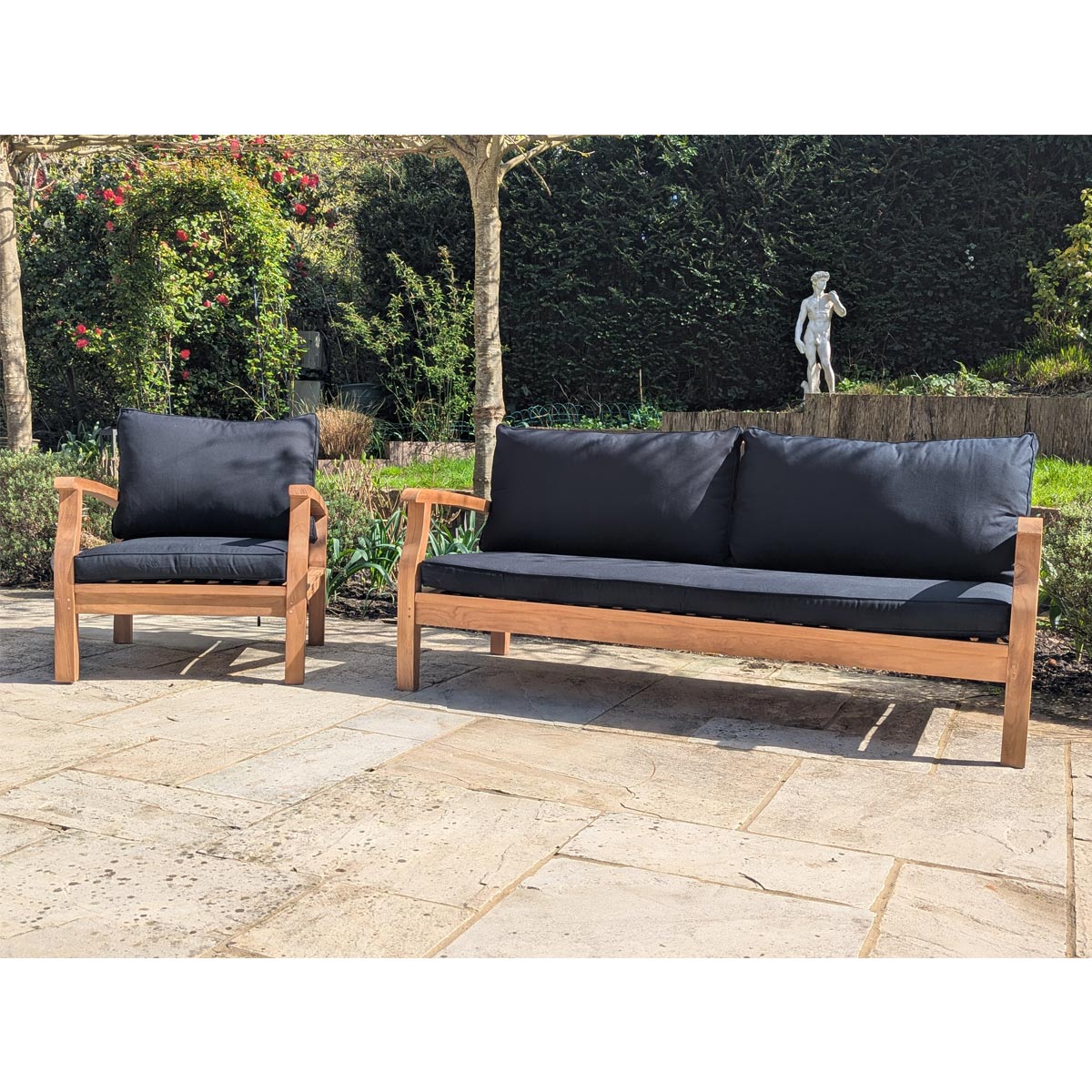 Outdoor furniture set with wooden frames and dark cushions on a stone patio.