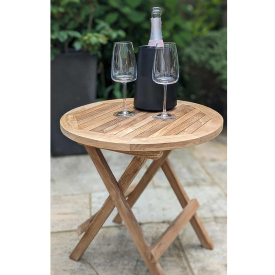 Wooden round folding table with two wine glasses and a bottle on a patio
