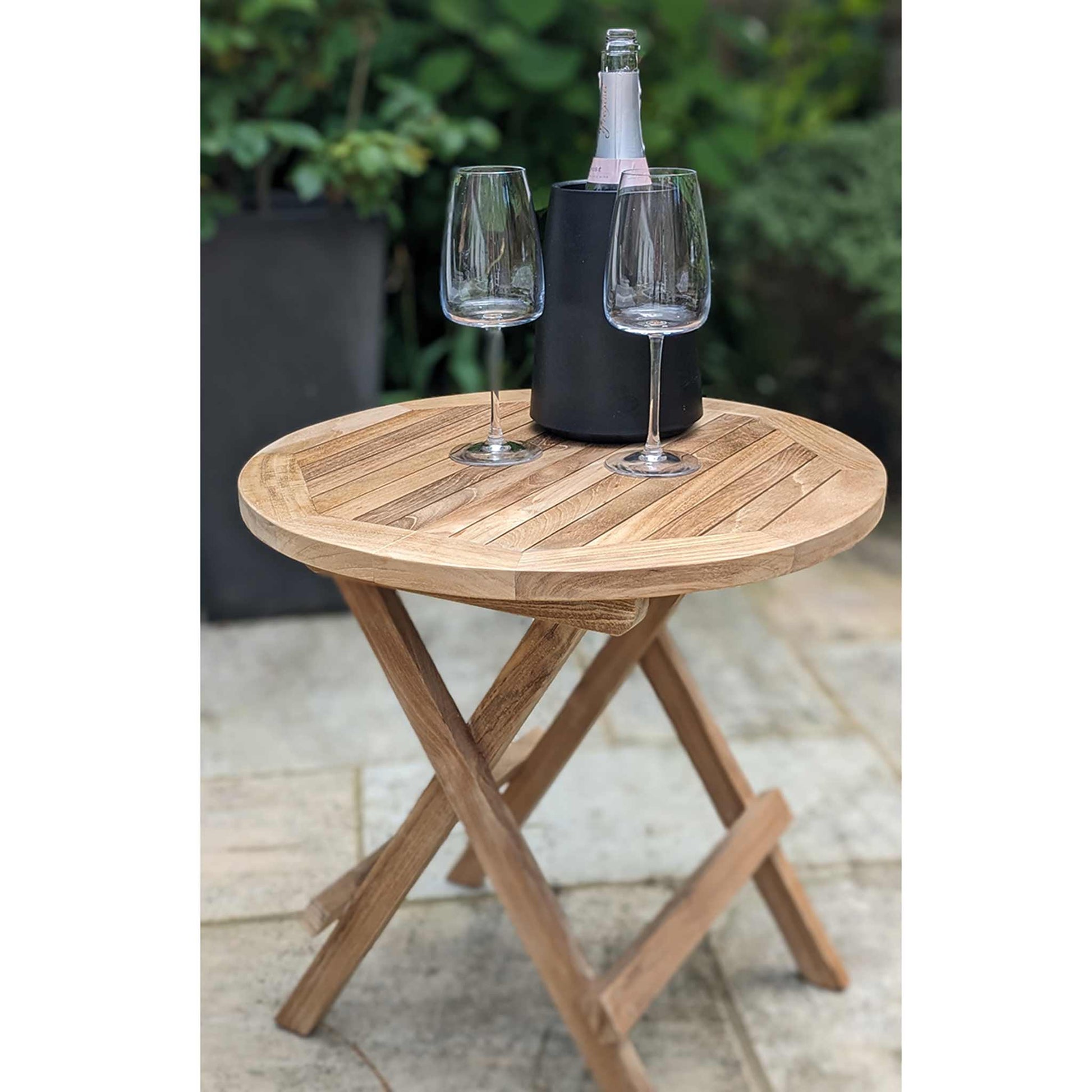 Wooden round folding table with two wine glasses and a bottle on a patio