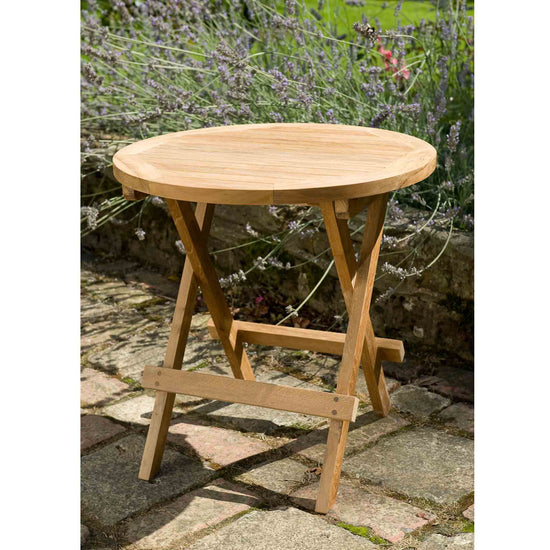 Wooden round folding table on a stone patio with lavender in the background