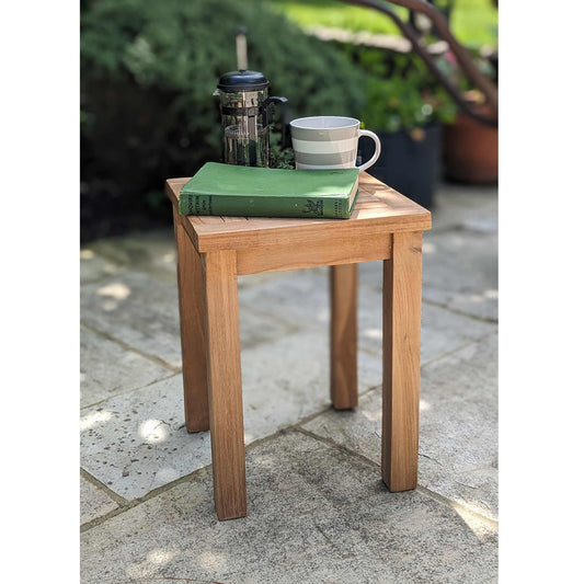 Small outside wooden side table with a book and cups on a stone patio