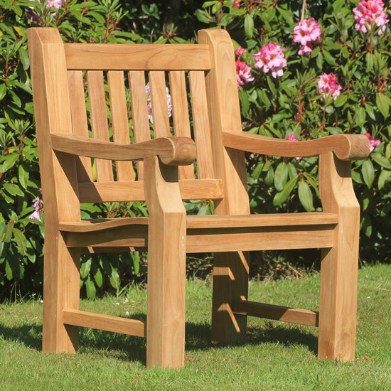 Teak garden wooden armchair, Great Maytham, on grass with pink flowers in the background