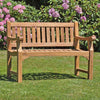 classic 2 seat teak garden bench, Sandhurst, in a garden setting with pink flowers and greenery