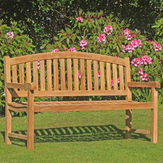 Wooden teak garden 3 seat curved back bench in a garden with pink flowers and greenery
