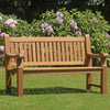 Heavy duty teak wooden bench in a garden with green grass and purple flowers in the background