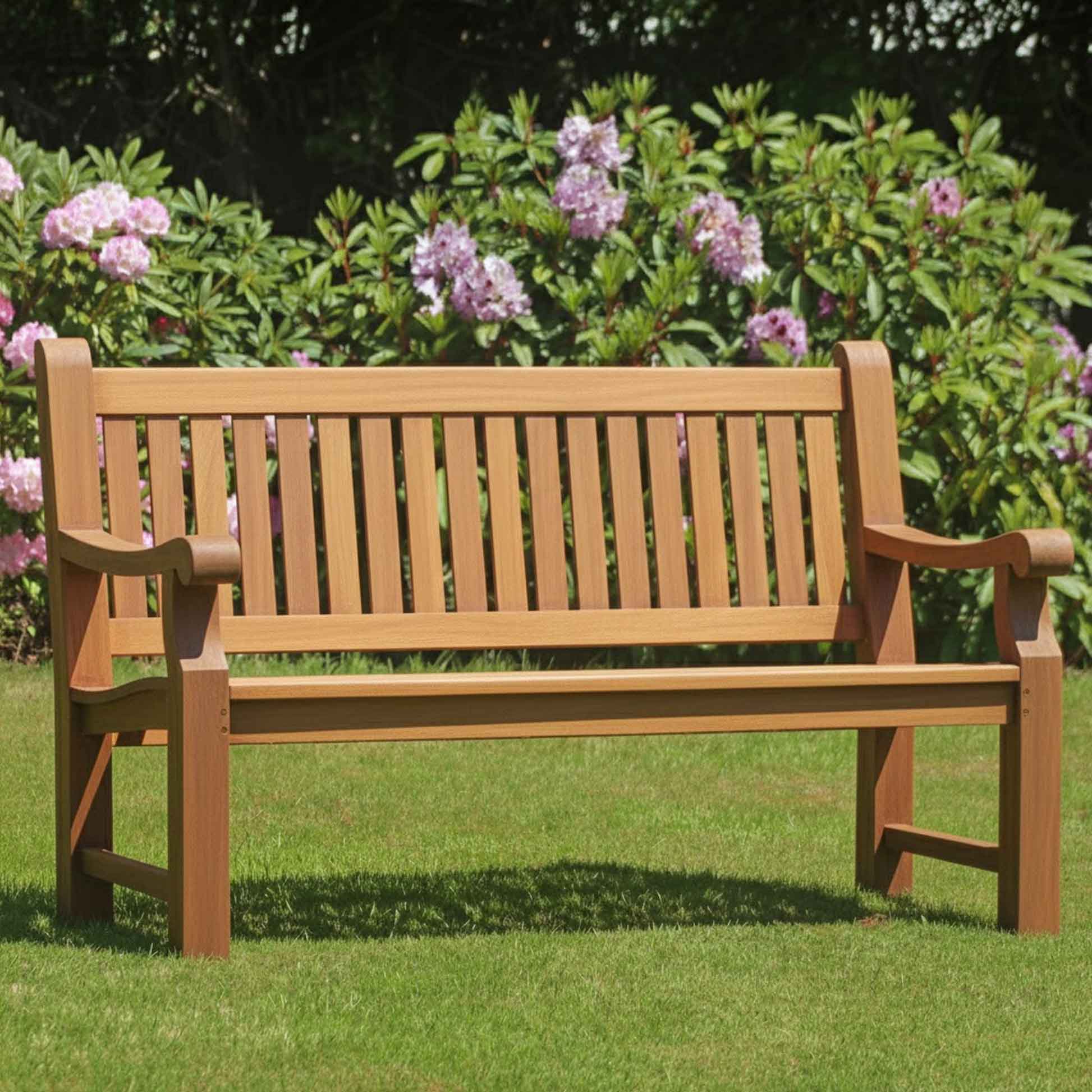 Heavy duty teak wooden bench in a garden with green grass and purple flowers in the background