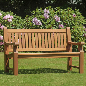 Heavy duty teak wooden bench in a garden with green grass and purple flowers in the background