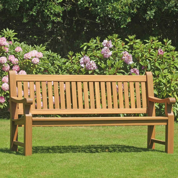 Wooden 4 seat teak garden Great Maytham  bench in a garden setting with purple rhododendrons in the background 