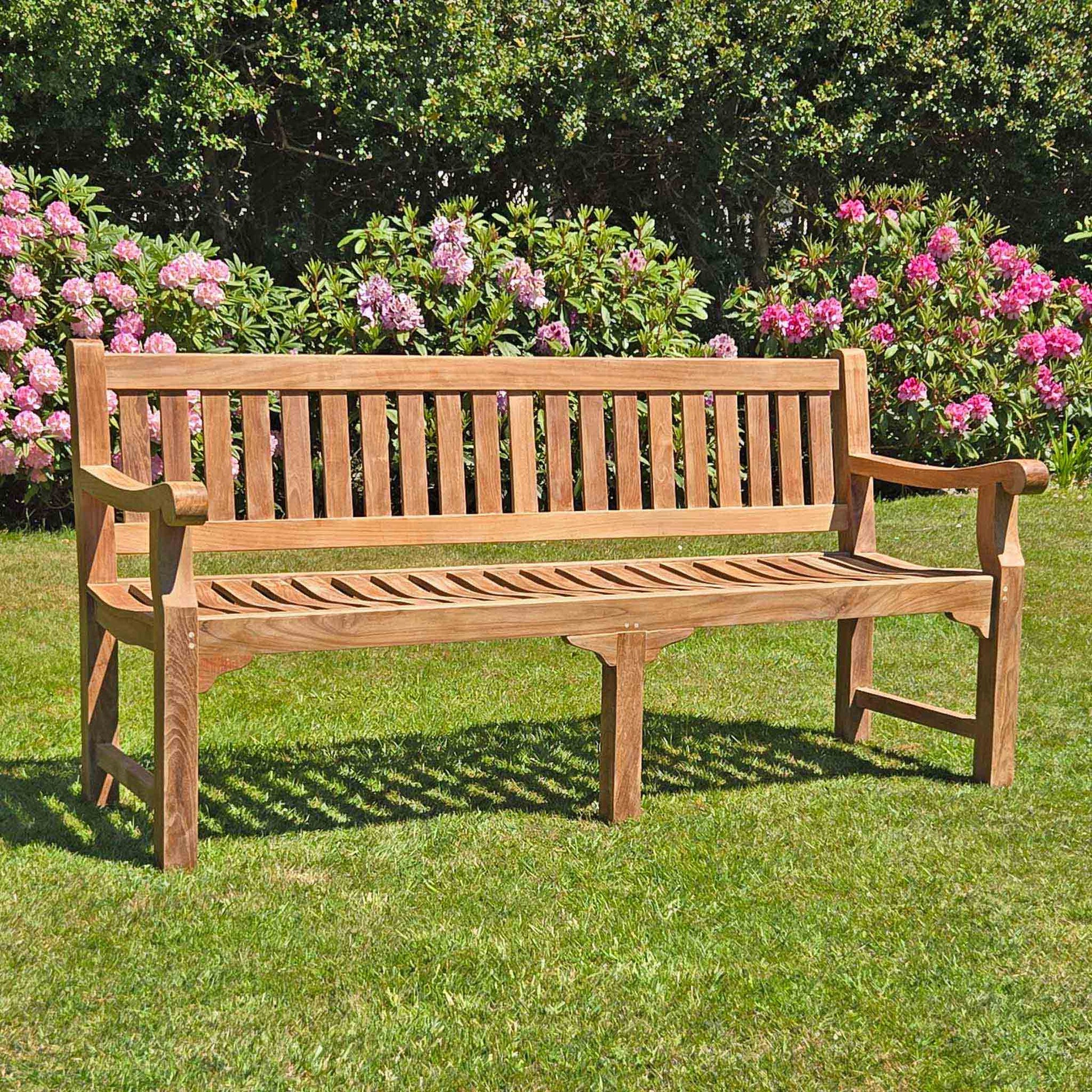 large 4 seat teak garden bench, Sandhurst, with scroll arms in a garden setting 