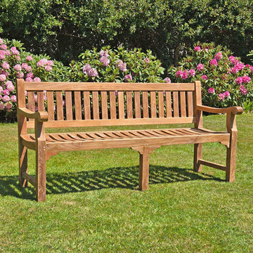 large 4 seat teak garden bench, Sandhurst, with scroll arms in a garden setting 