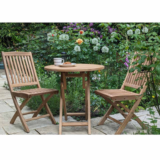 Wooden outdoor bistro style teak table with two chairs on a grassy area
