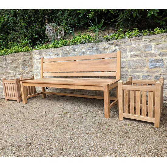 wooden teak garden bench and planter box on a stone pathway setting