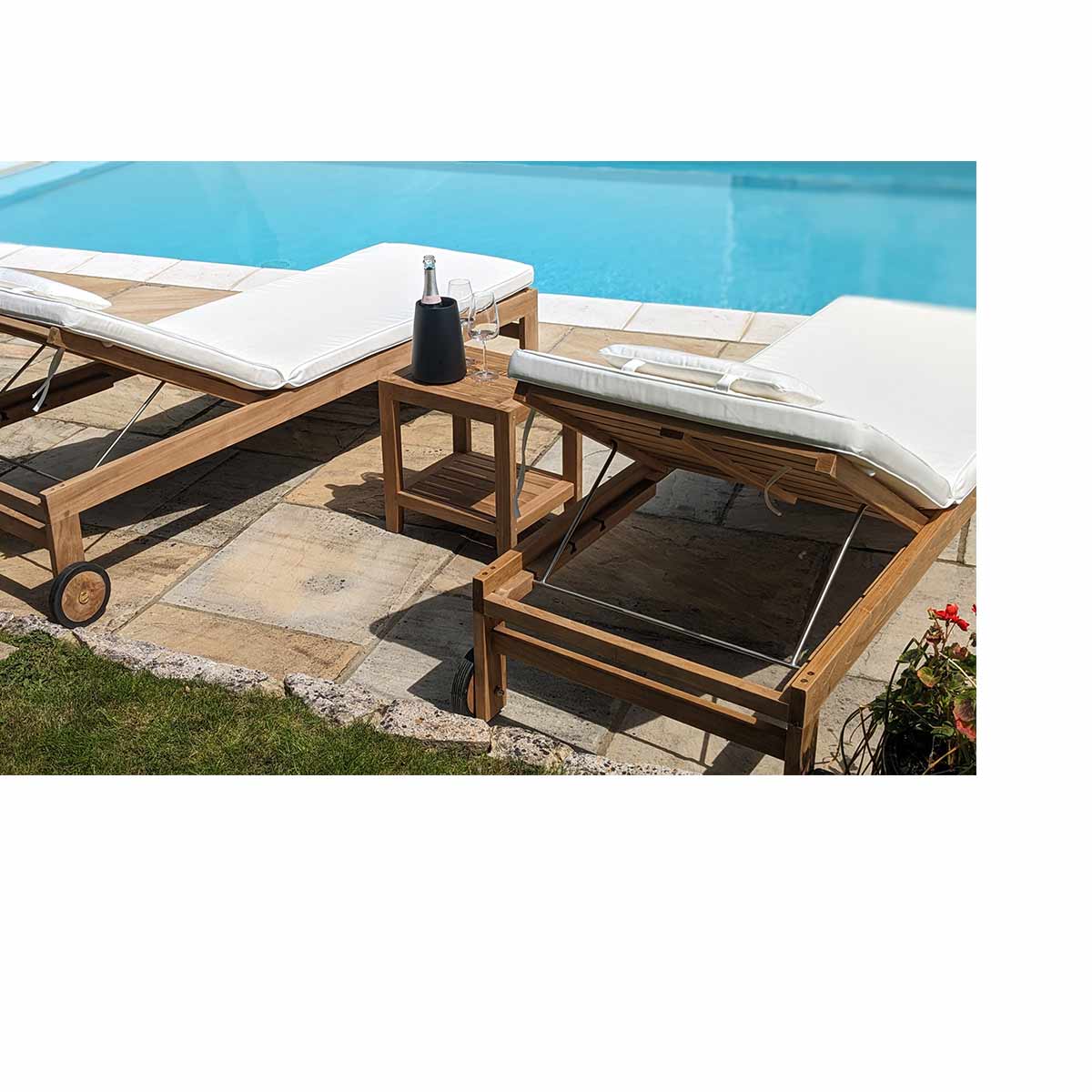 Two teak sun loungers with white cushions by a poolside.