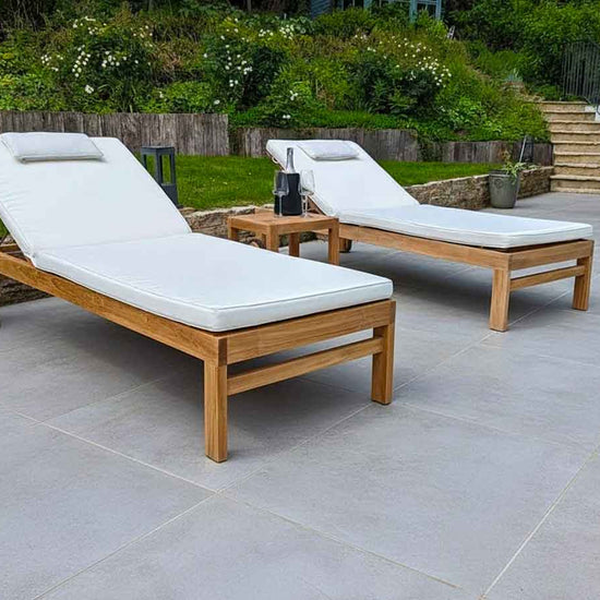 pair of teak garden sun loungers on grey ceramic tiles