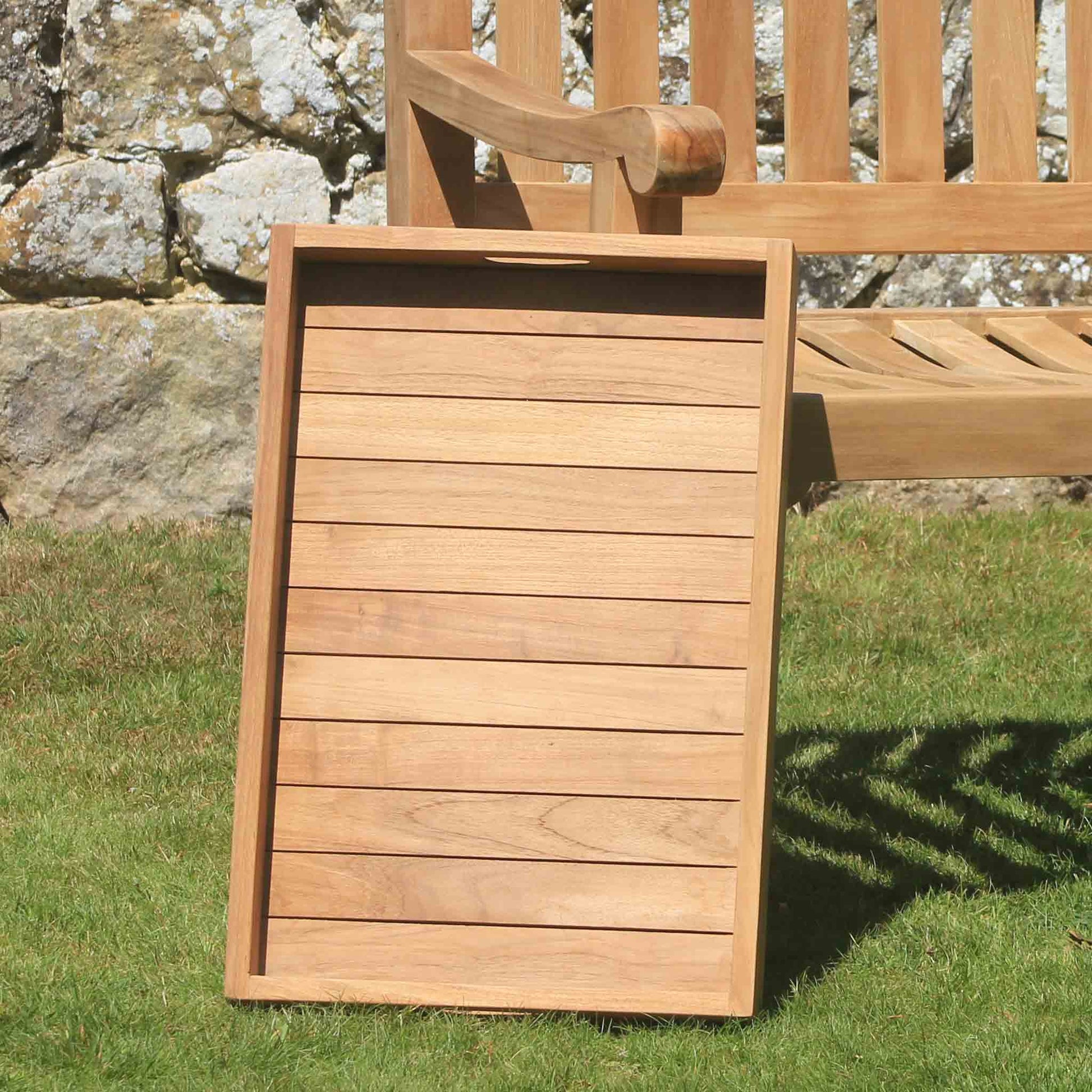 Wooden serving tray on grass with stone wall and bench in background