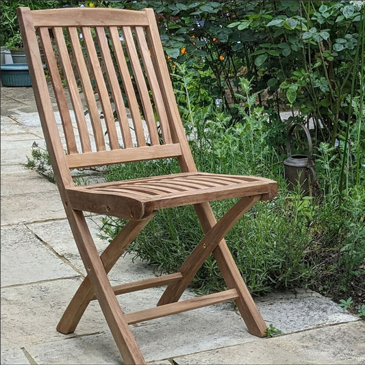 Wooden teak folding chair on a stone patio with greenery in the background