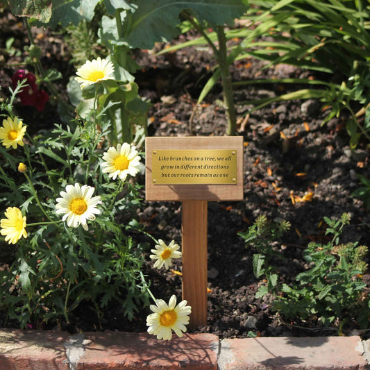 Teak garden marker with floral design and inspirational quote in a garden setting.